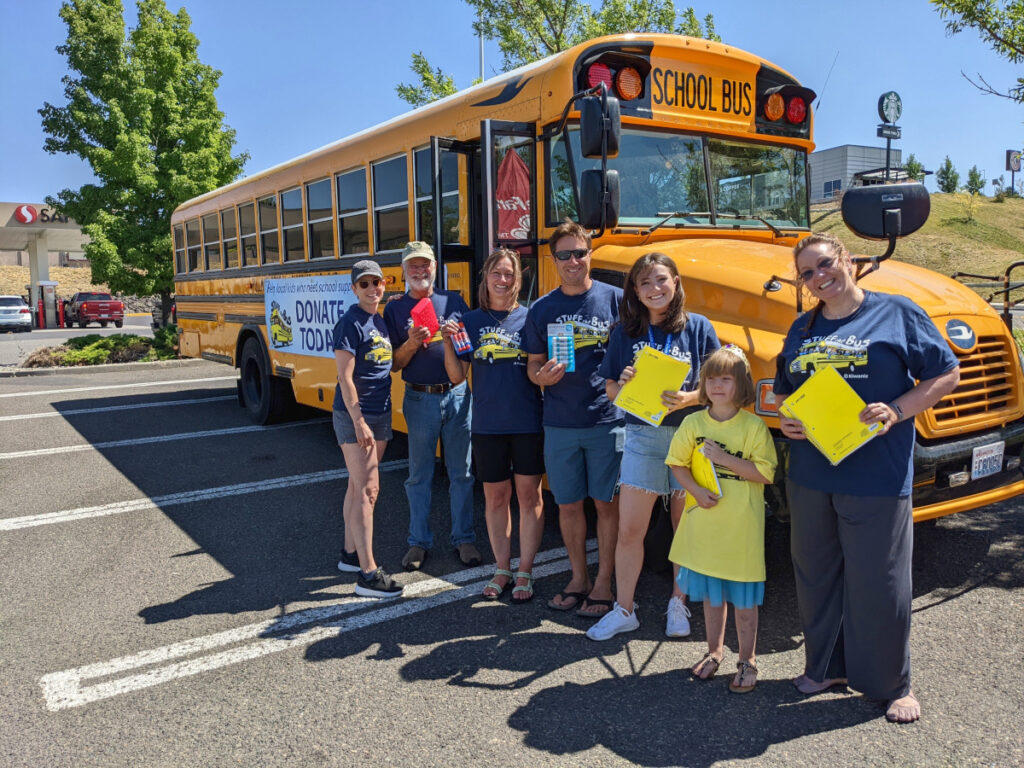Volunteers in front of a bus for Stuff the Bus school supplies drive in Pullman
