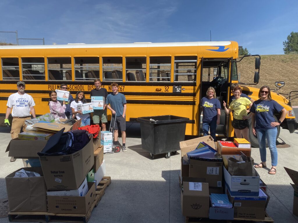 School supplies and volunteers in front of a school bus